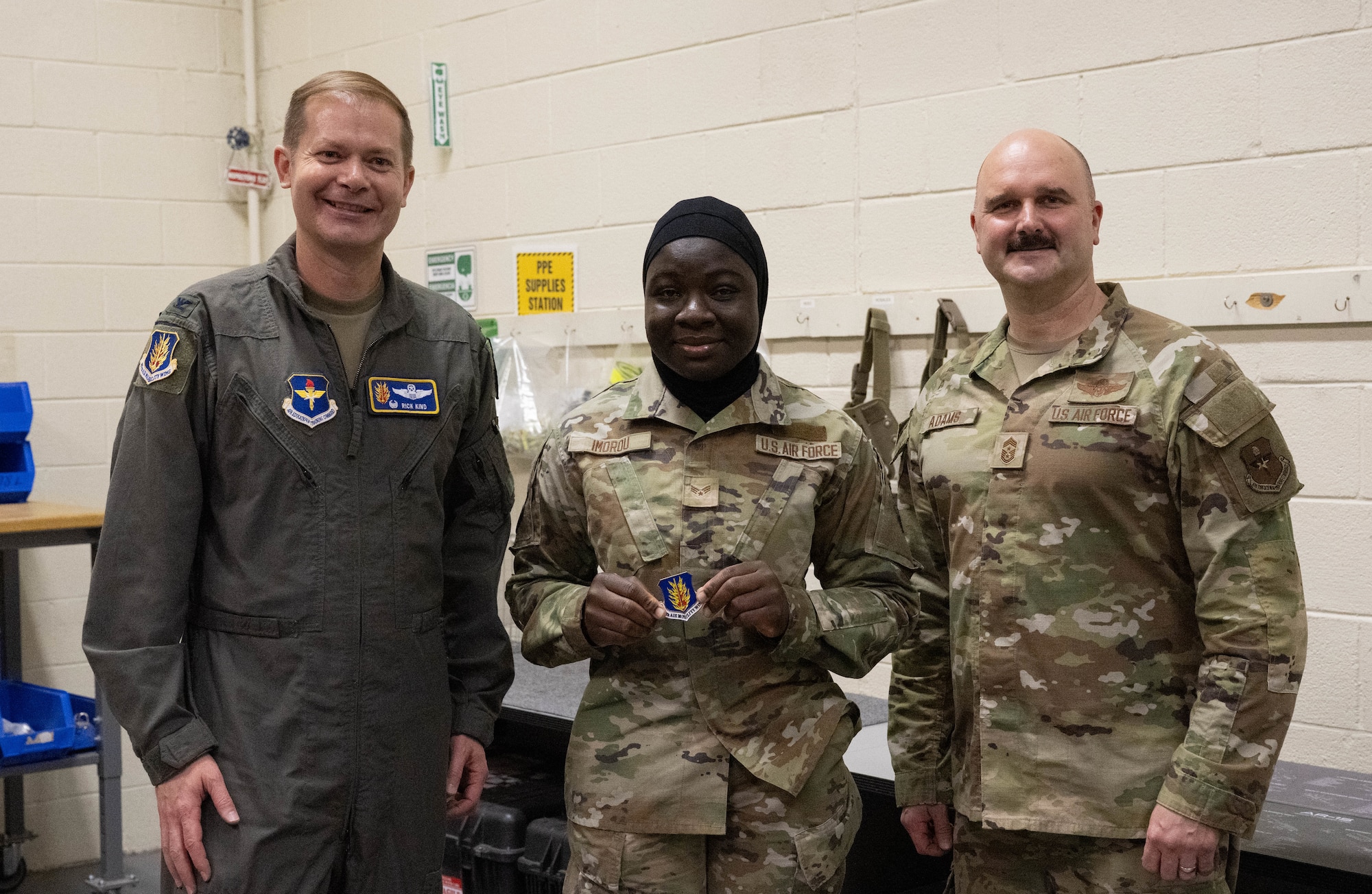 U.S. Air Force Col. Richard Kind, 97th Air Mobility Wing commander, left, and Chief Master Sgt. Jonny Adams, 97th AMW command chief, right, stands with Senior Airman Ouswatoy Mamoudou Imorou, 97th Logistics Readiness Squadron individual protective equipment journeyman, center, as she displays her coin at Altus Air Force Base, Oklahoma, Feb. 25, 2026. Kind recognized Imorou for her outstanding performance, professionalism and dedication to her duties. (U.S. Air Force photo by Airman 1st Class Emma Wright)