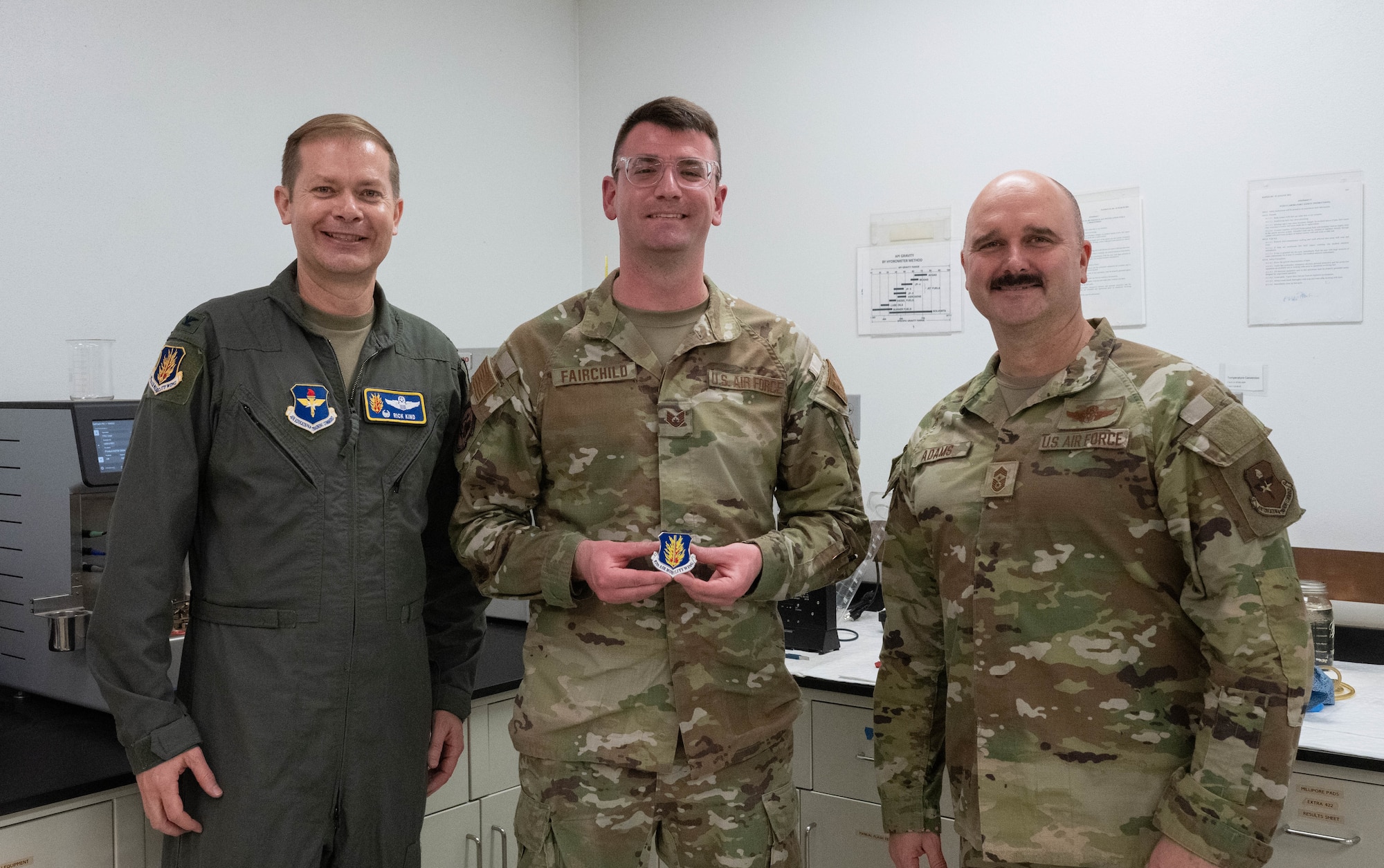 U.S. Air Force Col. Richard Kind, 97th Air Mobility Wing commander, left, and Chief Master Sgt. Jonny Adams, 97th AMW command chief, right, stands with Staff Sgt. Christopher Fairchild, 97th Logistics Readiness Squadron fuels laboratory non-commissioned officer in charge, center, as he displays his coin at Altus Air Force Base, Oklahoma, Feb. 25, 2026. Kind recognized Fairchild for his outstanding performance, professionalism and dedication to his duties. (U.S. Air Force photo by Airman 1st Class Emma Wright)
