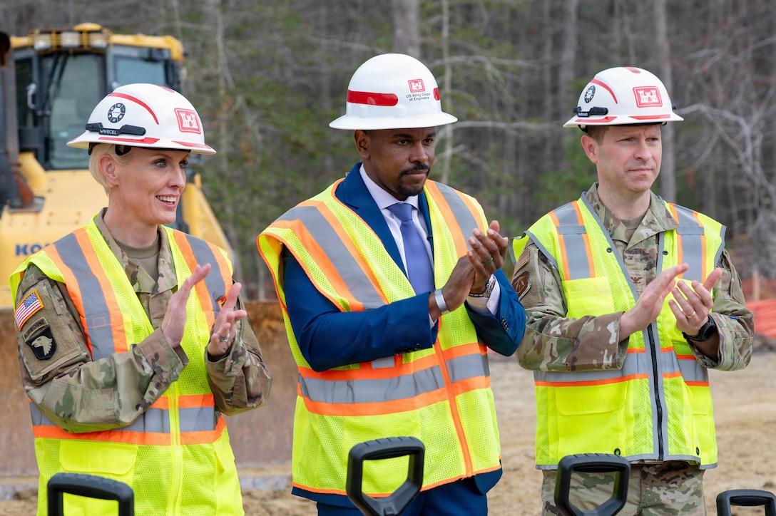 From left, U.S. Army Col. Laura Hutchinson, 733d Mission Support Group commander, Phillip Jones, mayor of Newport News and U.S. Air Force Col. Stephen Anderson, 633d Air Base Wing commander stand side by side clapping with hard hats on and yellow vests.