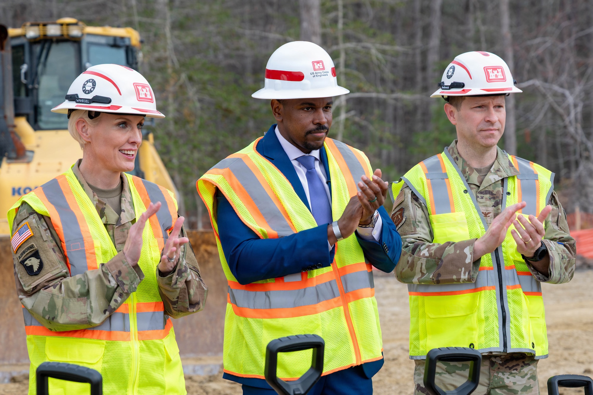 From left, U.S. Army Col. Laura Hutchinson, 733d Mission Support Group commander, Phillip Jones, mayor of Newport News and U.S. Air Force Col. Stephen Anderson, 633d Air Base Wing commander stand side by side clapping with hard hats on and yellow vests.