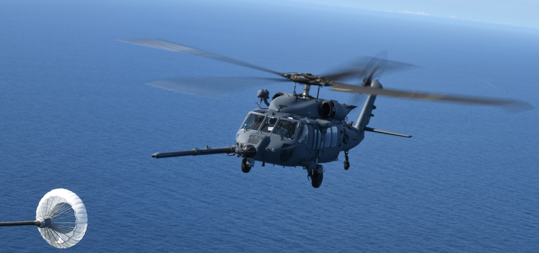 A U.S. Air Force HH-60W Jolly Green II helicopter approaches a drogue for aerial refueling
