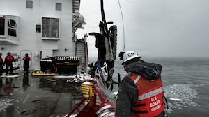 A snowmobile is hoisted onto a Coast Guard cutter that is in open waters and winter conditions.