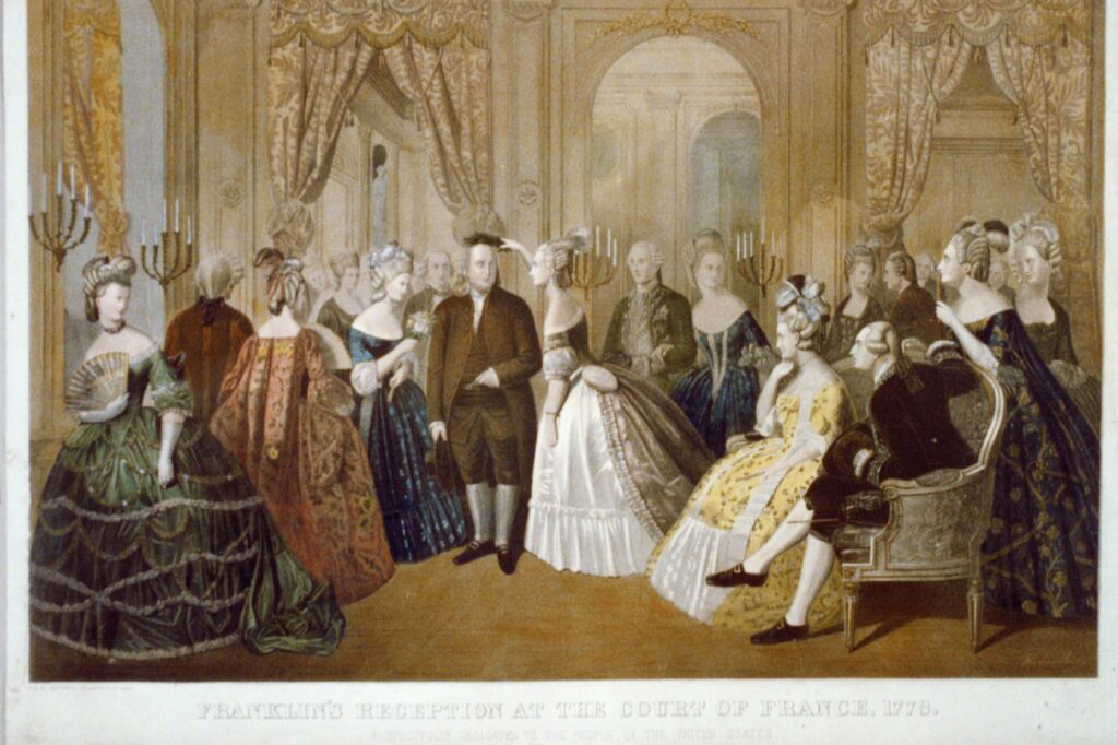 People dressed in formal 18th-century attire attend to a man in similar attire inside a ballroom.