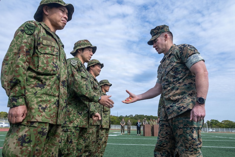 U.S. Marine Corps Colonel Chris Niedziocha, commanding officer of the 31st Marine Expeditionary Unit, gives a coin to Japan Ground Self-Defense Force members, during the closing ceremony for Iron Fist 26, at Camp Hansen, Okinawa, Japan, March 9, 2026. Iron Fist is an annual bilateral exercise designed to increase interoperability and strengthen the relationships between the U.S Marine Corps, U.S. Navy and JGSDF. The 31st MEU is a persistent, combat credible force operating aboard the ships of the Tripoli Amphibious Ready Group in the U.S. 7th fleet area of operations, routinely interacting and operating with our allies and partners to contribute to deterrence, security, crisis response, and combat operations in the Indo-Pacific region. (U.S. Marine Corps photo by Cpl. Eric Reyes)