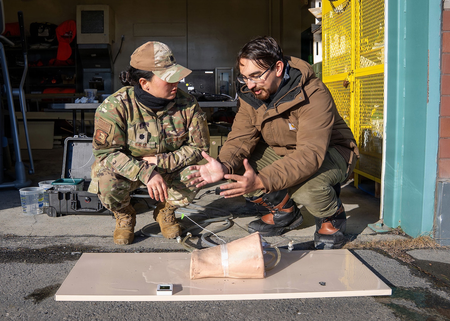 Andres Martinez Murillo, lead biomedical engineer for Naval Medical Research Unit (NAMRU) San Antonio, explains stability testing on the novel SynDaver thermal, bleeding manikin thigh to U.S. Air Force Lt. Col. Kaitlin Salle at the Kodiak Coast Guard Clinic in Kodiak, Alaska during Arctic Edge 2026, Feb. 26. The novel manikin thigh is meant to keep the circulating ‘blood’ heated to normal body temperature so that researchers can see decompensation of bleeding while exposed to extreme cold. NAMRU San Antonio, part of Navy Medicine Research & Development, conducts gap-driven combat casualty care, craniofacial, and directed energy research in support of Navy, Marine Corps and joint U.S. warfighter health readiness and lethality while engaged in routine and expeditionary operations. (U.S. Navy Photo by MC1 Abigayle Lutz/Released)