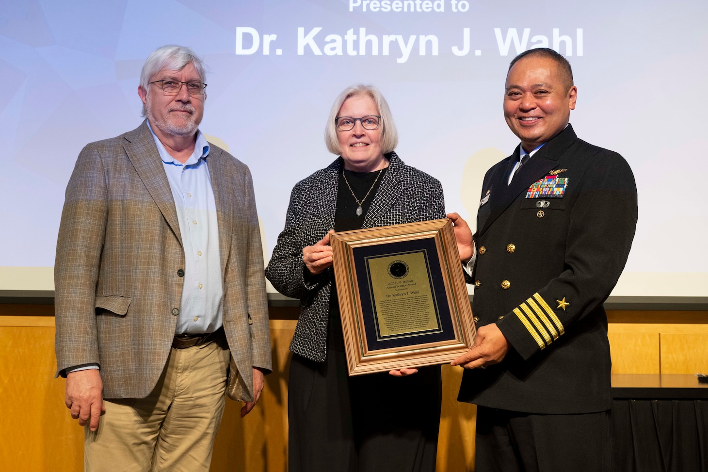Kathryn Wahl (center), Ph.D., U.S. Naval Research Laboratory (NRL) Surface Chemistry branch head, receives the 2025 E.O. Hulbert Annual Science Award from Dr. Bruce Danly (left), NRL director of research, and CAPT Randy Cruz, NRL commanding officer, in Washington, D.C., March 6, 2026. Wahl received the award for her significant advances in measurement, observation, and understanding of interfacial contacts. (U.S. Navy photo by Sarah Peterson) RELEASED