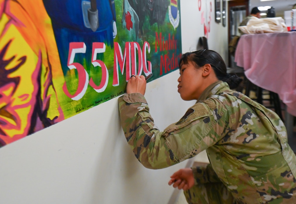 Staff Sgt. Alyssa Adasa, 55th Medical Support Squadron, signs her name onto the 55th Medical Group's new mural located in the Heritage Hall at the Ehrling Bergquist Clinic, Feb. 20, 2026.