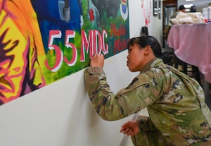 Staff Sgt. Alyssa Adasa, 55th Medical Support Squadron, signs her name onto the 55th Medical Group's new mural located in the Heritage Hall at the Ehrling Bergquist Clinic, Feb. 20, 2026.