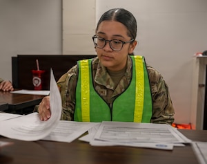 An Airman wearing a reflective vest flips through paperwork.