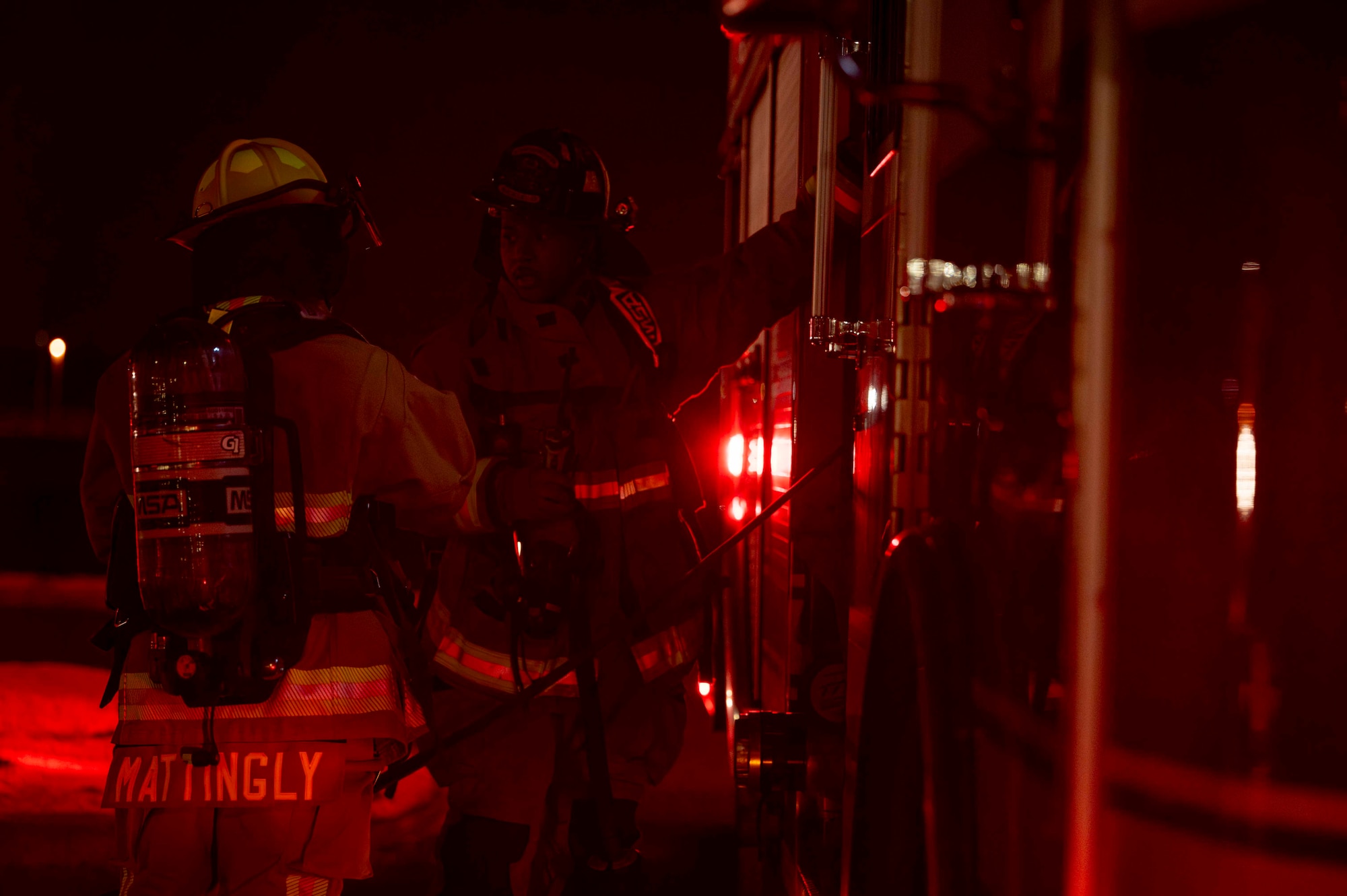 Two firefighters stand by a fire truck.