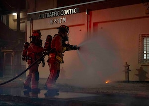 Two firefighters spray water at a simulated fire.