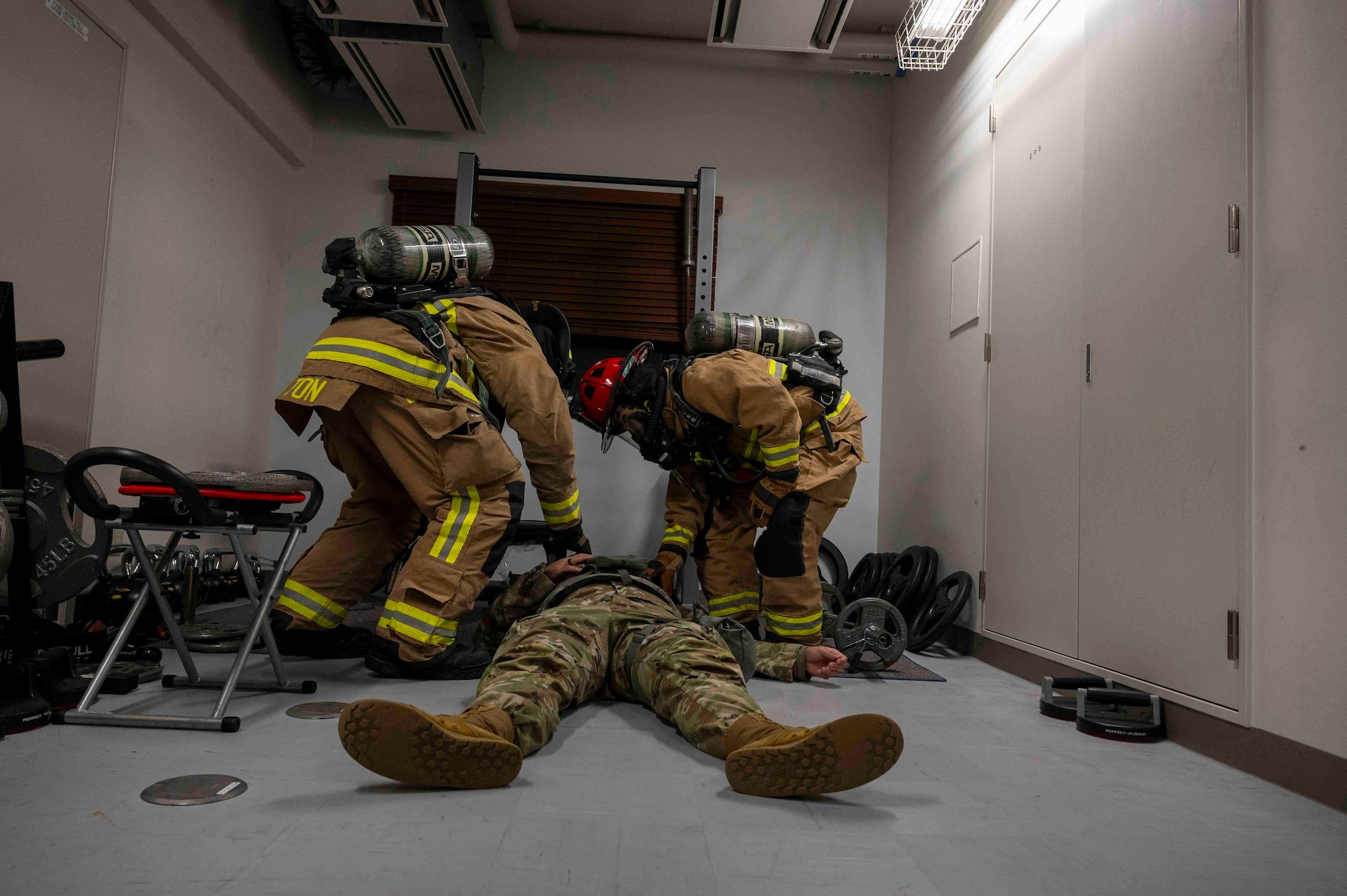 Two firefighters assist an Airman lying on the floor.