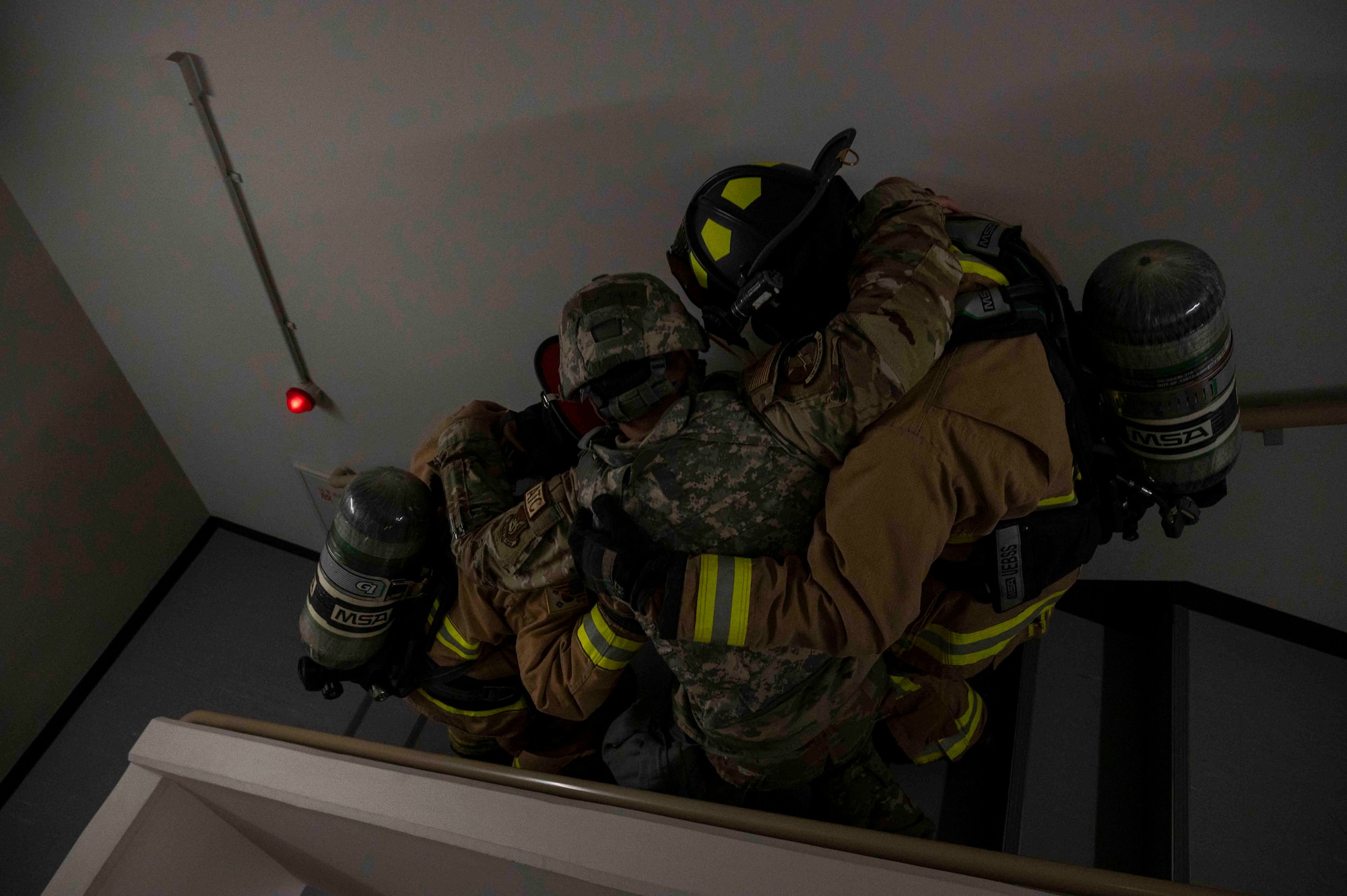 Two firefighters assist an Airman going downstairs.
