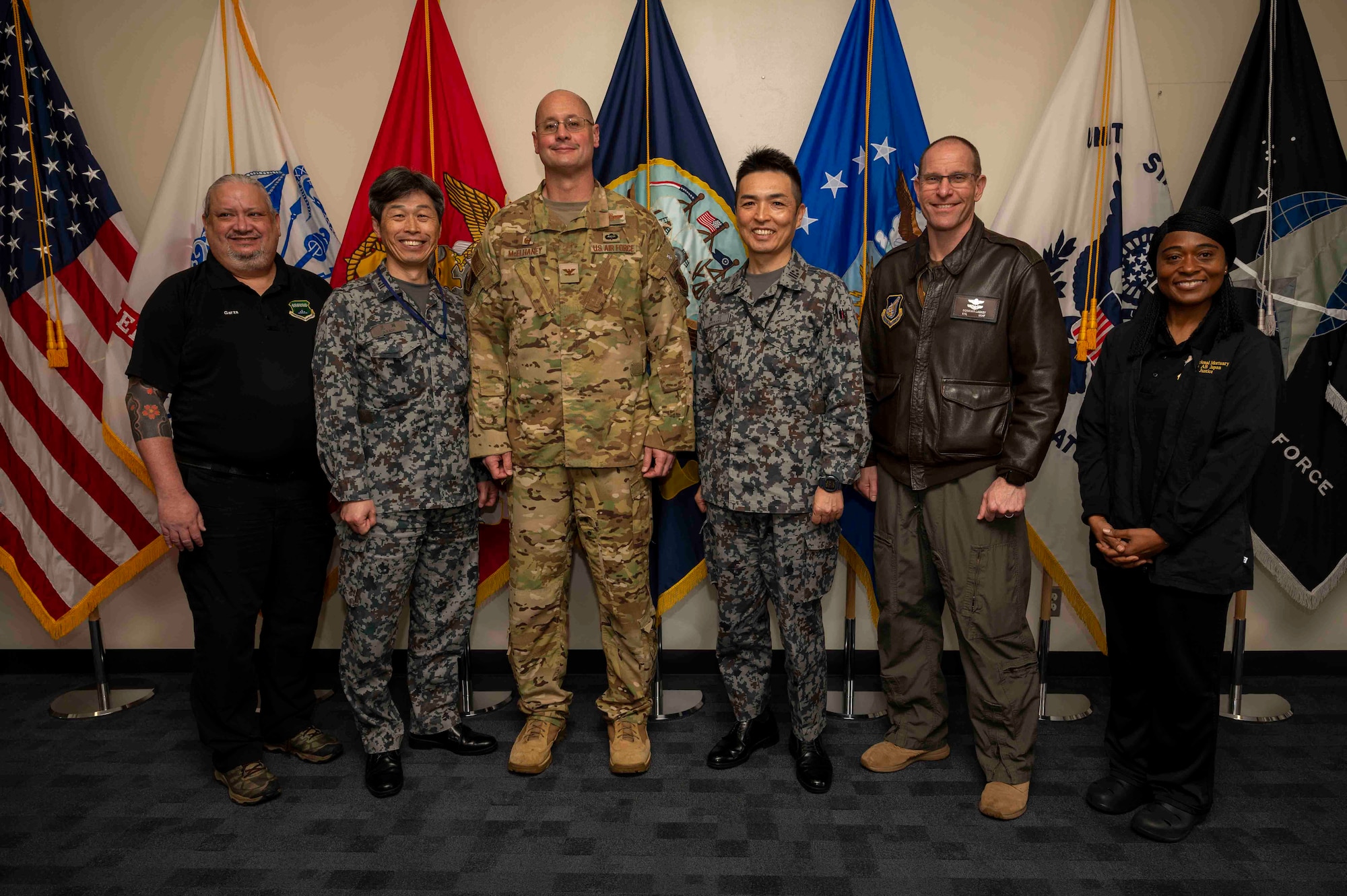 Military members and civilians pose for a group photo in front of flags.