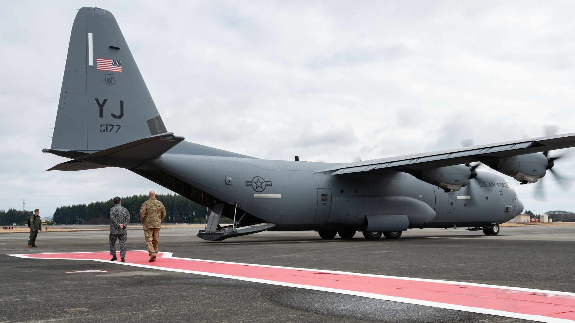 Two military members walk towards the back of a C-130J Super Hercules aircraft.