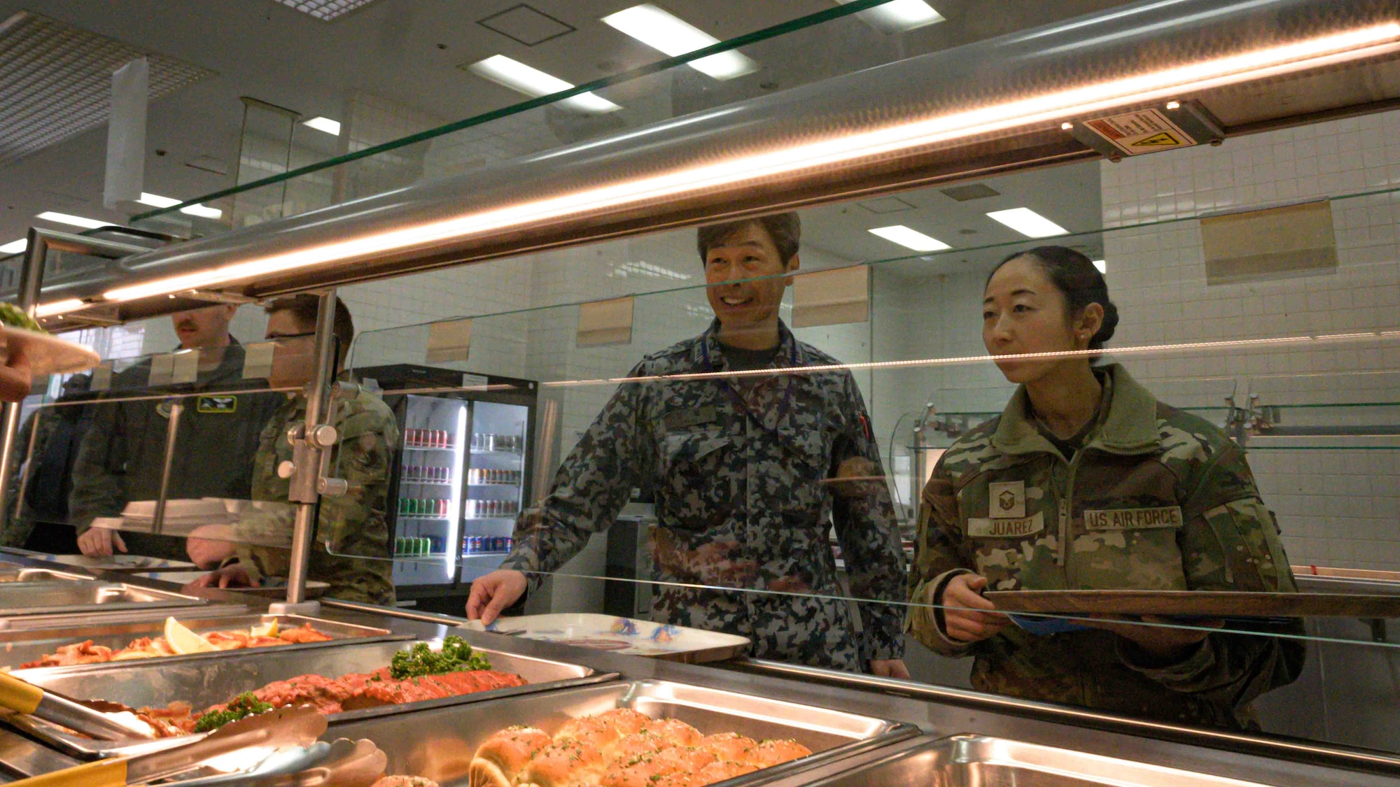 A Japan Air Self-Defense Force member and a U.S. Air Force Airman look at a food display in a dining facility.