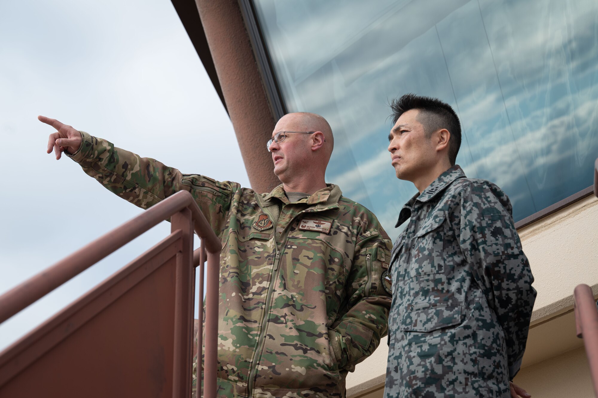 An Air Force military member points as a Japan Air Self-Defense Force military member looks on.