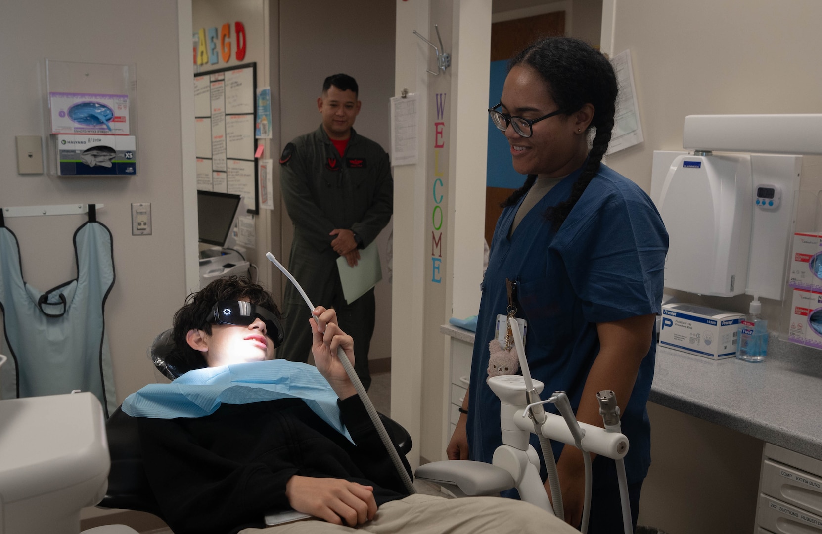 Aurelio (left), son of Tech. Sgt. Brian Cruz (center), 343rd Reconnaisance Squadron section chief of cyber support operations, holds a saliva ejector tool as a 55th Dental Squadron dental assistant stands by during Children's Dental Day at the Ehrling Bergquist clinic, March 6, 2026. The 55th DS provided a variety of dental services including flouride treatments and cleaning. (U.S. Air Force photo by Daniel Martinez)