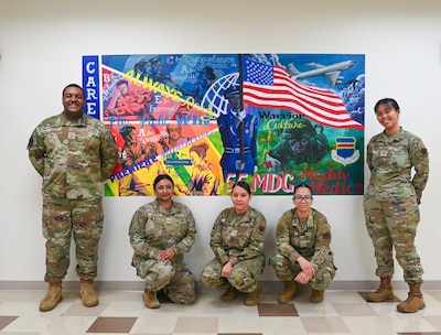 Volunteers pose in front of the 55th Medical Group's new mural located in the Heritage Hall at the Ehrling Bergquist Clinic, Mar. 17, 2026. More than 10 volunteers from across the clinic collaborated to complete the painting.