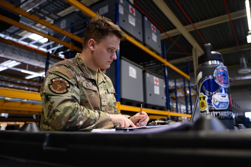 A person looks at a computer and records information on a sheet of paper.