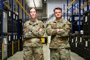 Two people pose for a photo inside a warehouse.