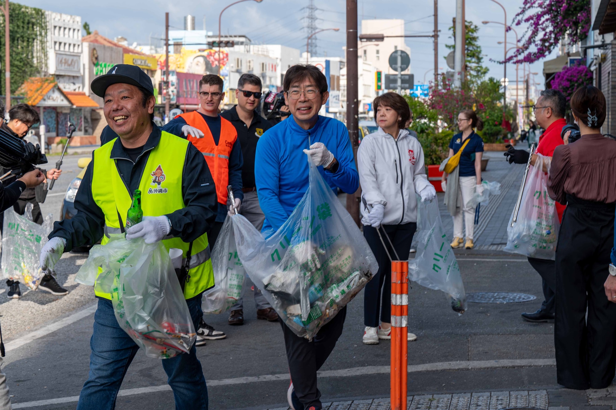 volunteers and civic leaders hold trash bags while walking down the street