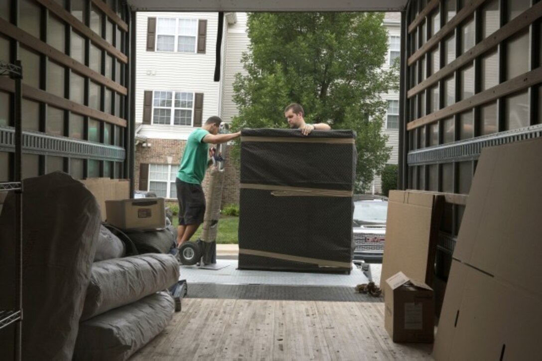 Individuals unload furniture from the back of a moving truck.