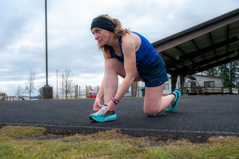 A woman wearing athletic gear bends down to tie her sneakers.