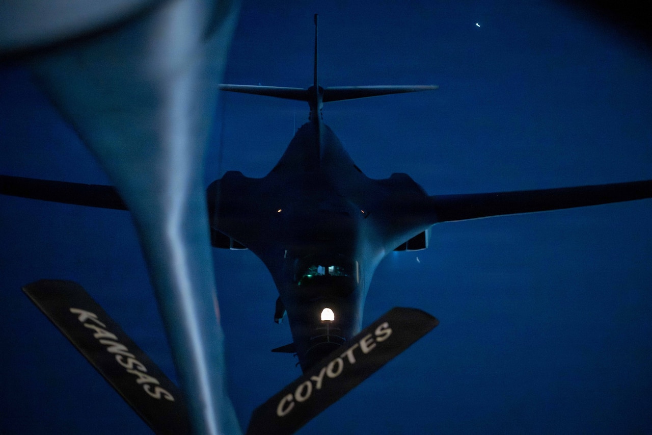 An aircraft’s boom extends to another aircraft while flying in a night sky.