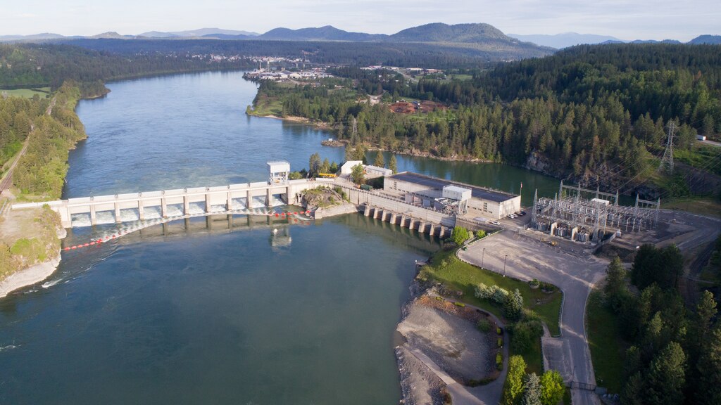 Aerial photo of a dam with 11 spillway gates, a hydropower generating unit, and a lake in front of it.