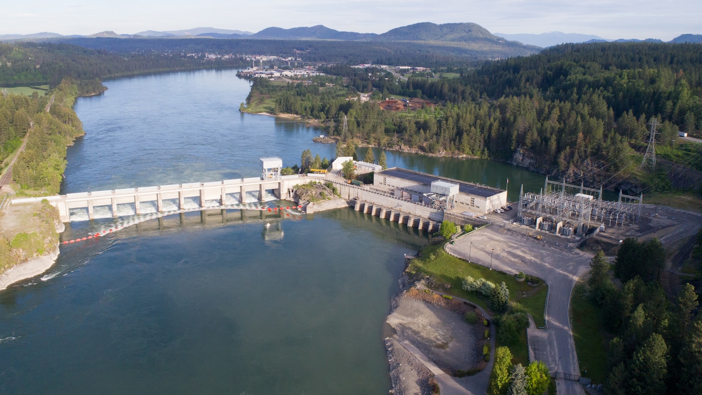 Aerial photo of a dam with 11 spillway gates, a hydropower generating unit, and a lake in front of it.