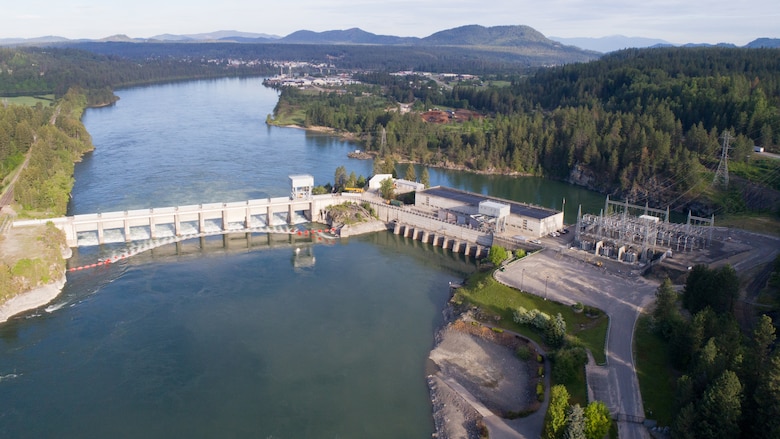 Aerial photo of a dam with 11 spillway gates, a hydropower generating unit, and a lake in front of it.