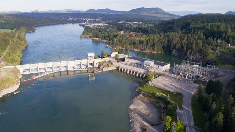 Aerial photo of a dam with 11 spillway gates, a hydropower generating unit, and a lake in front of it.