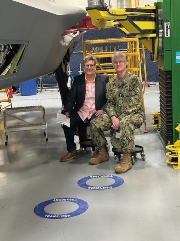 Two people seated next to partially built aircraft fuselage