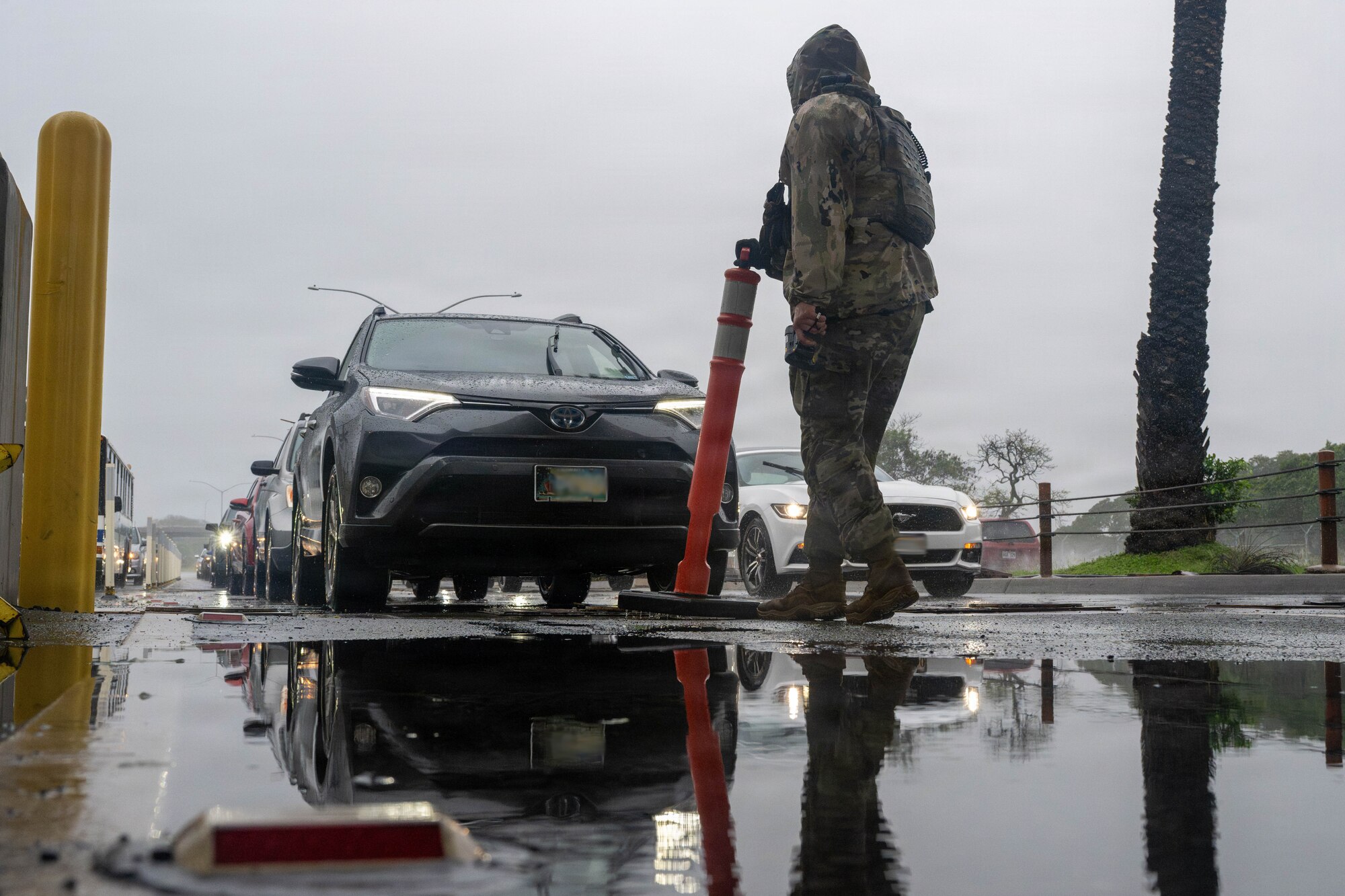 An Airman in rain gear moves a cone in front of a vehicle.