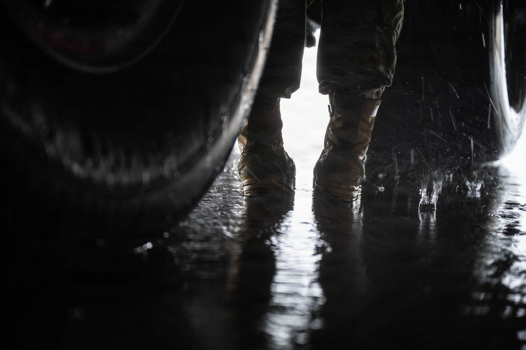 A photo of an Airman's wearing boots drenched in rain while in between a large set tires attached to a large U.S. Air Force aircraft.