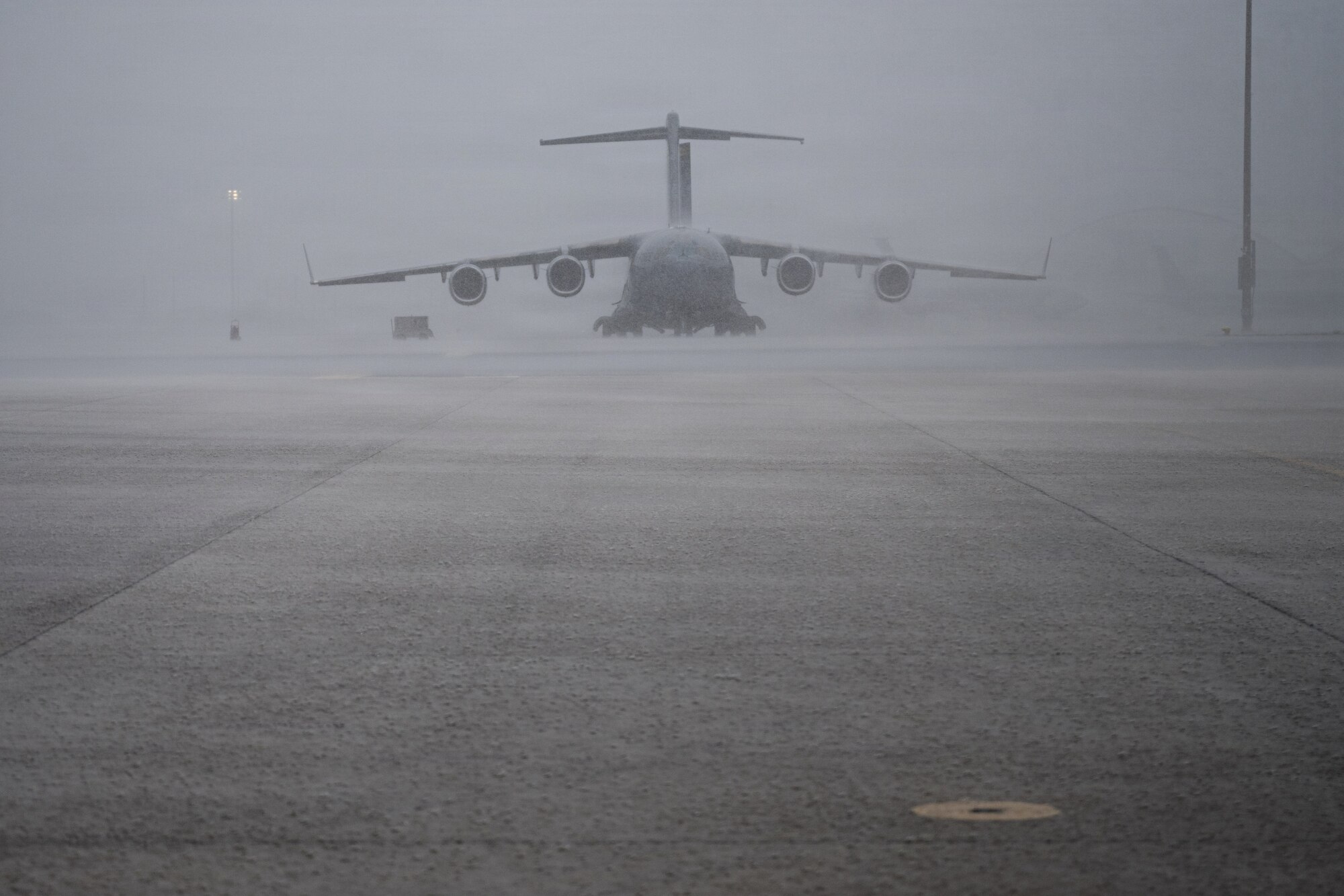 A photo of a large U.S Air Force aircraft sits as a large of rain down pours onto the flight line.