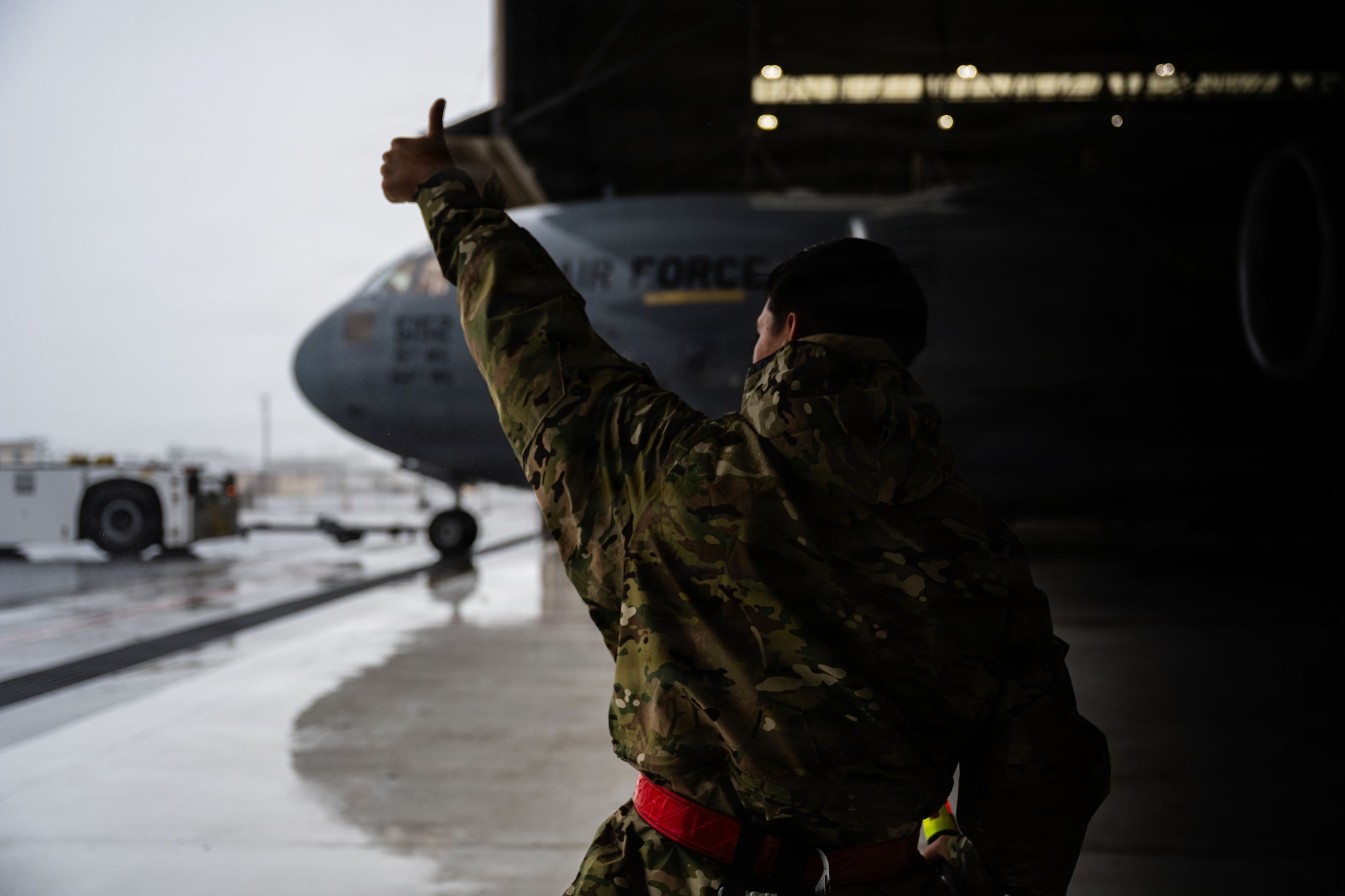 An Airman with one arm raised while holding a thumbs up towards a U.S. Air Force aircraft.