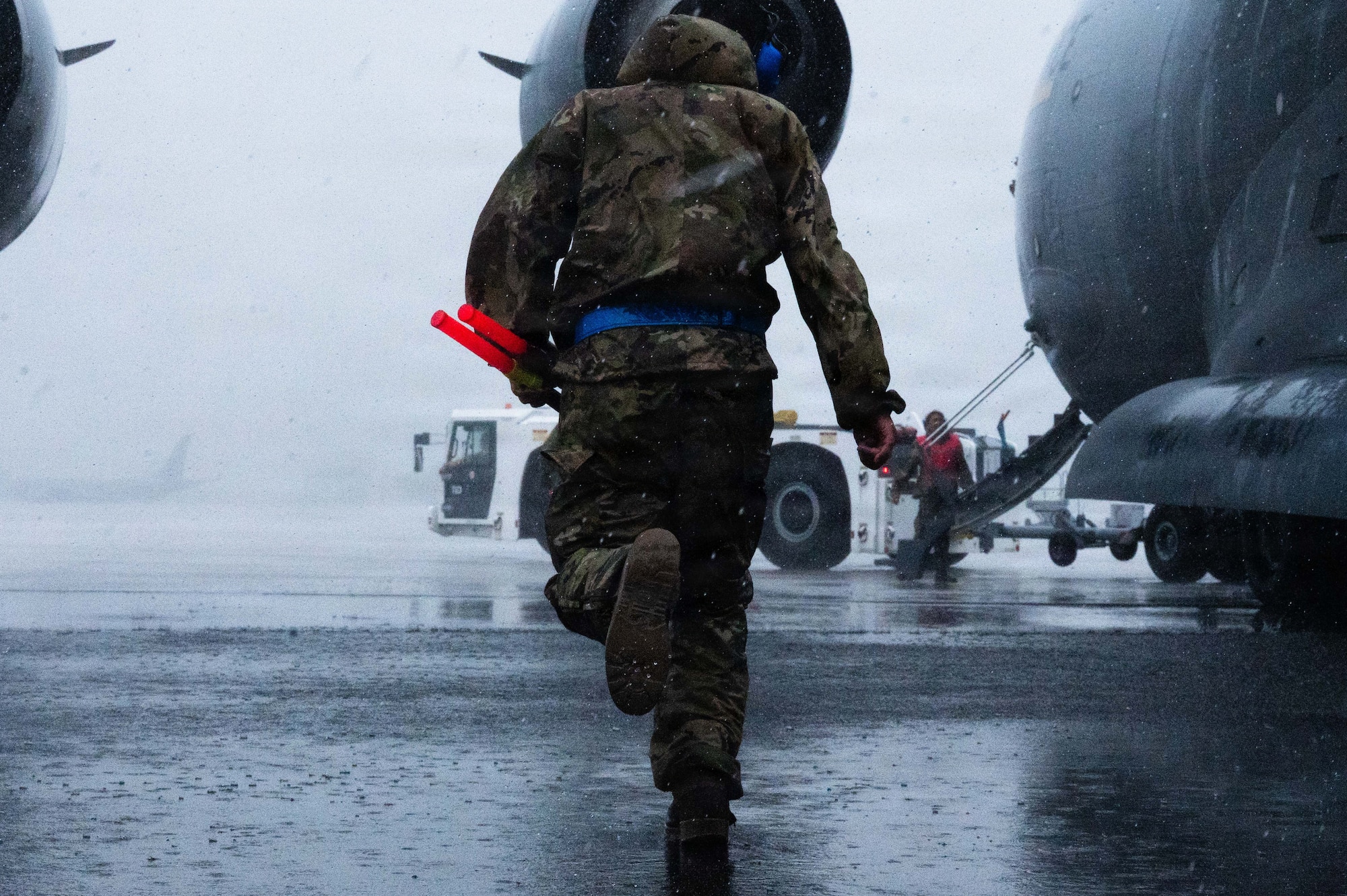 An Airman in rain gear runs towards an aircraft during routine maintenance.