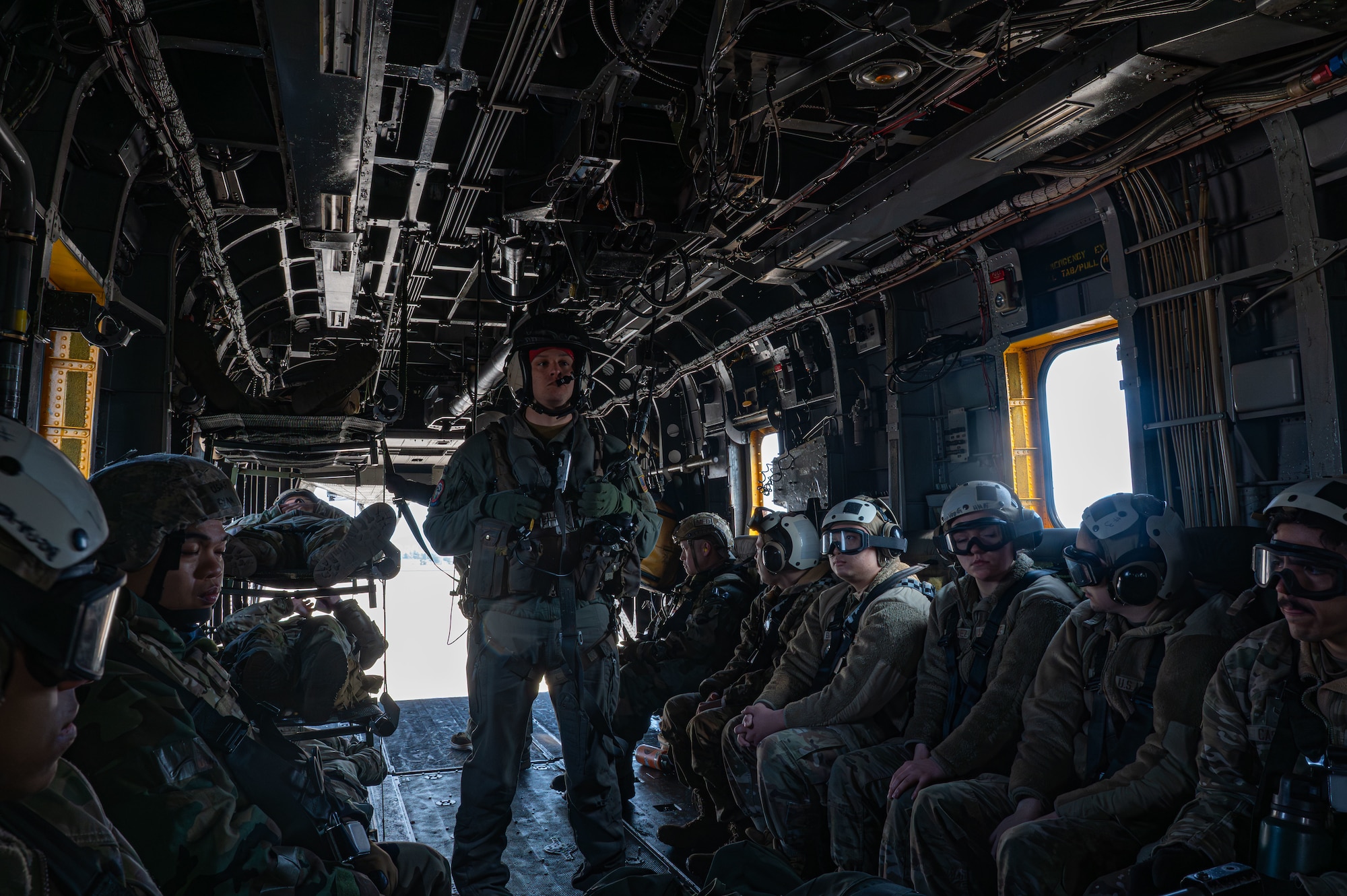 Naval Aircrew stands in a helicopter while Airmen sit around him.