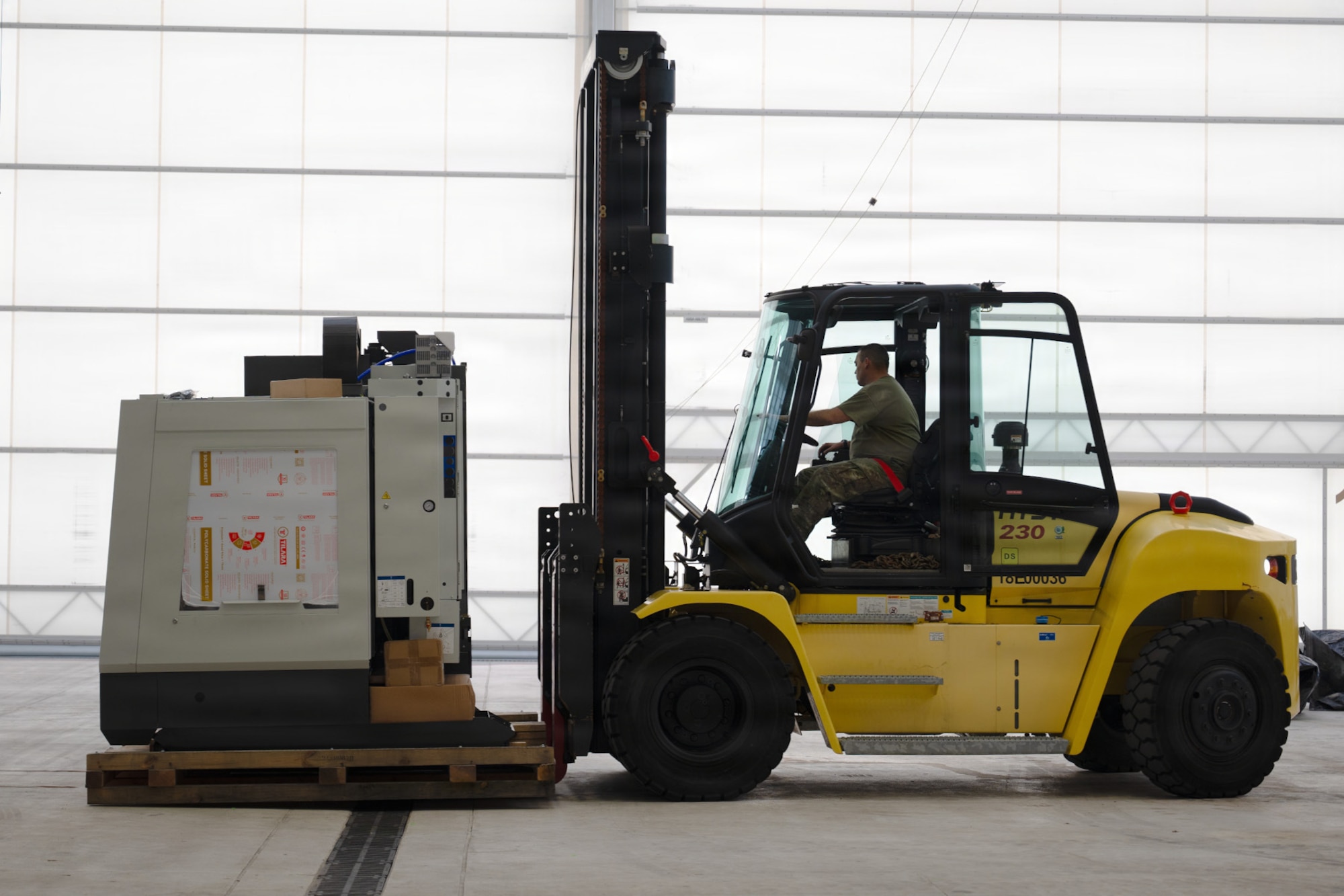 An Airman loads a skid onto a forklift inside a warehouse.