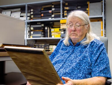 Dr. Hughes, AMCOM historian, gazes upon an old photo, reflecting on the end of a remarkable era as her retirement marks the beginning of a new chapter.