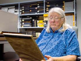 Dr. Hughes, AMCOM historian, gazes upon an old photo, reflecting on the end of a remarkable era as her retirement marks the beginning of a new chapter.