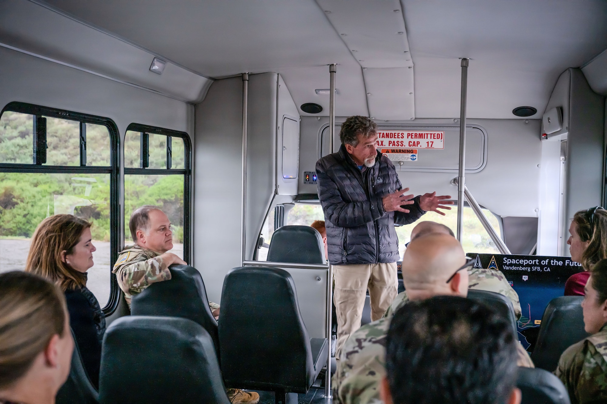 a person standing inside of a bus points out an object outside and explains its significance to others on the bus
