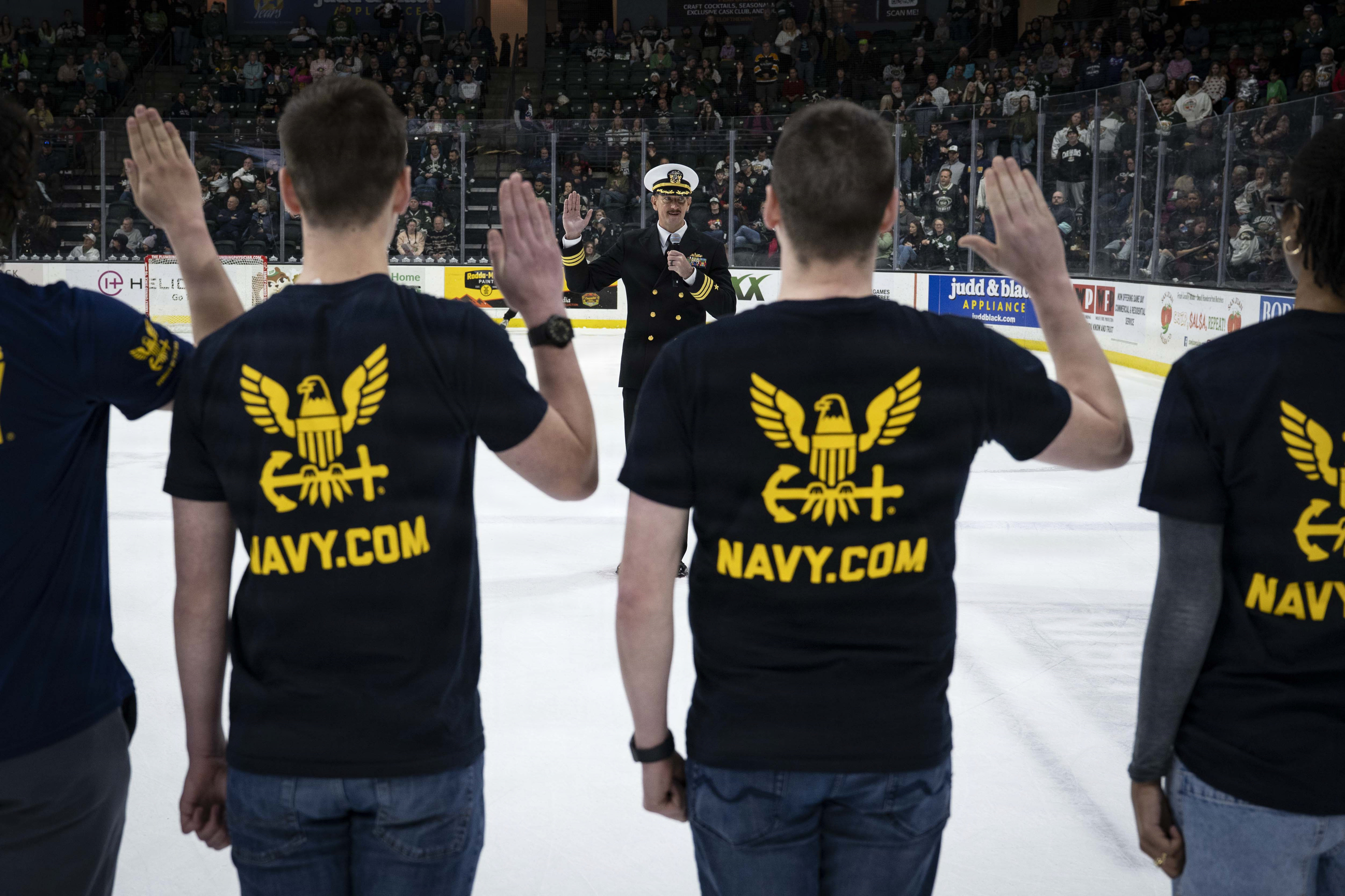 On the ice at Angel of the Winds Arena, Cmdr. Michael Ferrell administers the oath of enlistment to 15 future Sailors, marking the start of their journey with the U.S. Navy.