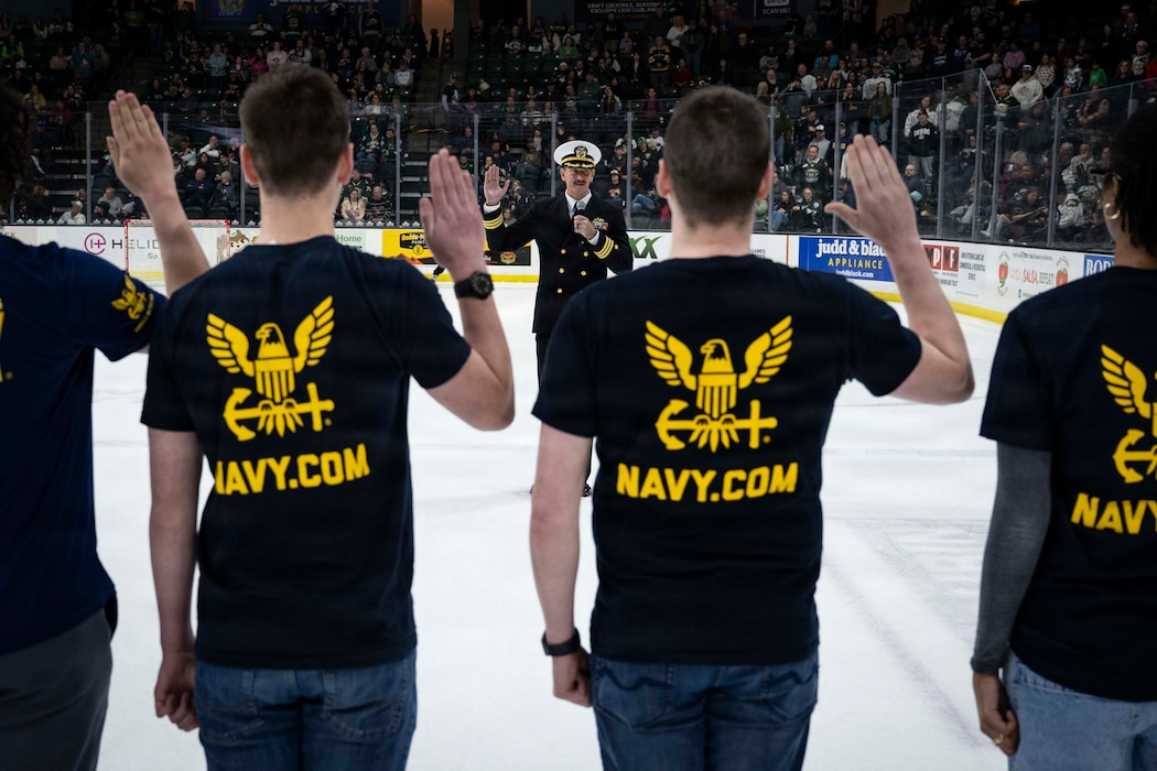 On the ice at Angel of the Winds Arena, Cmdr. Michael Ferrell administers the oath of enlistment to 15 future Sailors, marking the start of their journey with the U.S. Navy.