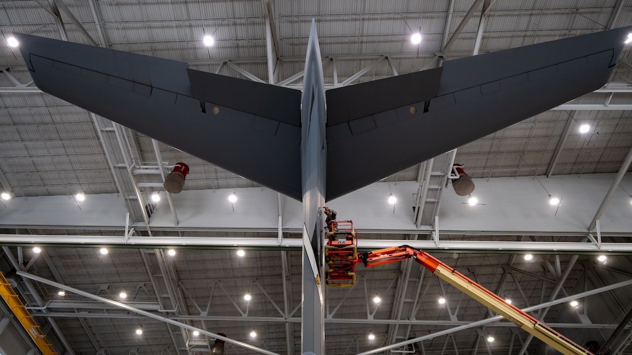 A tail of a C-17 is visible with an Airman in a cherry picker working on it