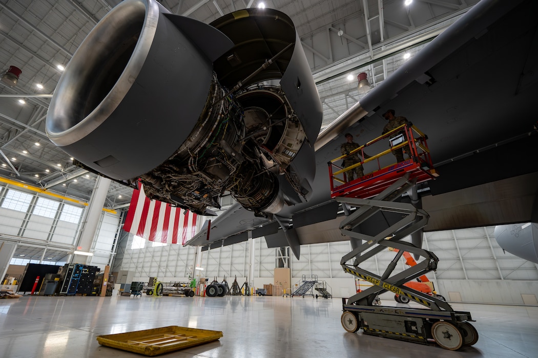 An engine is exposed with two Airmen on a scissor lift