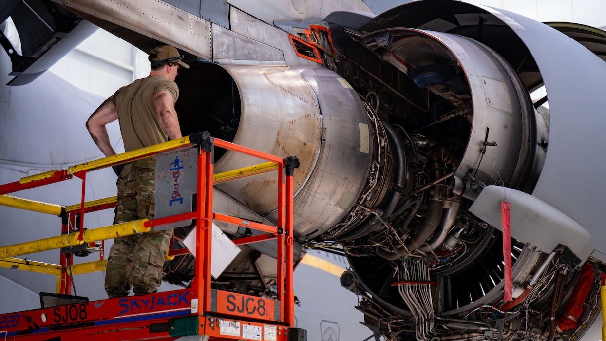 An Airman stands behind an exposed engine