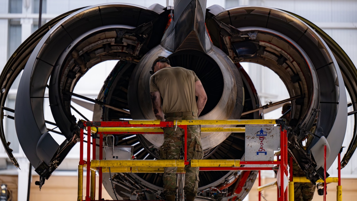 An engine is exposed with an Airman standing behind it
